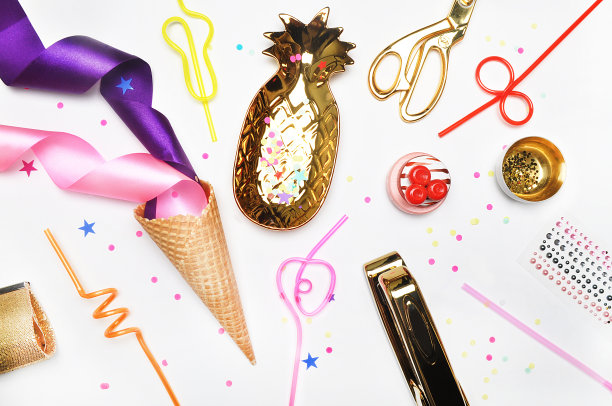 魅力风格背景，平铺。黄金和派对物品:鸡尾酒管苹果，梨，螺旋形，冰淇淋蛋筒，黄金化妆包，黄金菠萝，订书机，剪刀，糨糊。桌面。查看表。图片下载