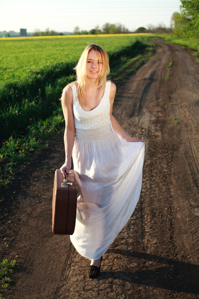 美丽的女孩穿着白色长裙，带着手提箱在乡下图片下载