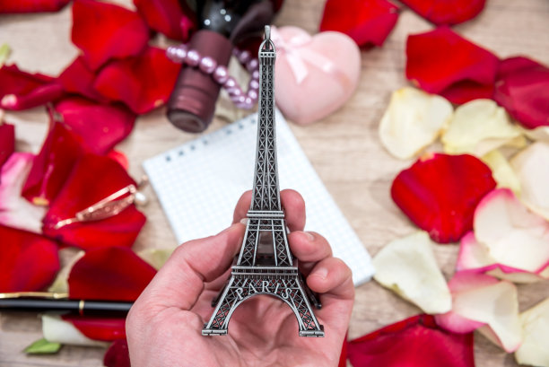 手拿埃菲尔铁塔模型，背景是玫瑰花瓣图片下载
