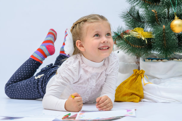 小女孩戴着圣诞帽，在圣诞树旁给圣诞老人写信图片下载