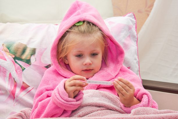 小女孩在床上穿着暖和的睡袍看着温度计图片下载
