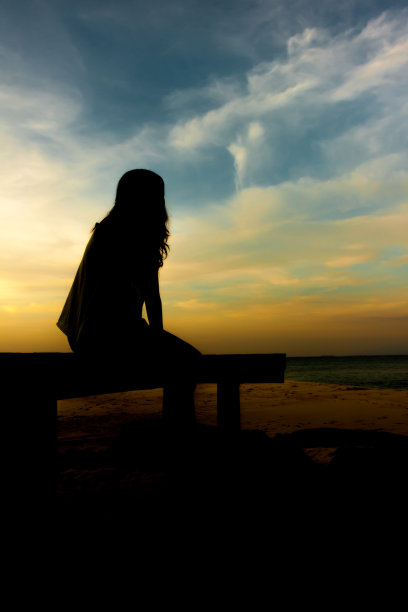 黄昏的天空下，女人们的剪影坐在海边的桥上图片下载