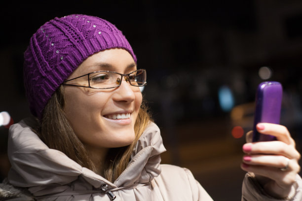 女人穿着冬天的衣服在城市里使用智能手机图片下载