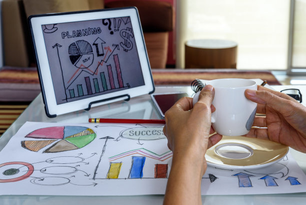 手拿咖啡杯，桌上放着平板电脑图片下载