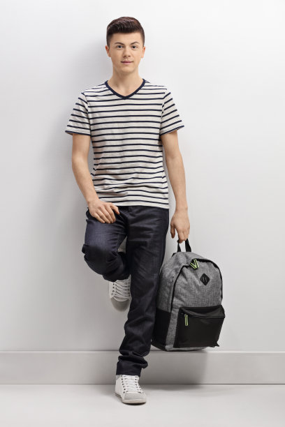 十几岁的男孩拿着背包靠在灰色的墙上图片下载