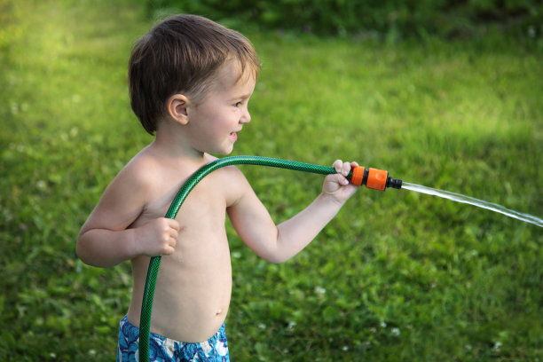 男孩在绿草的背景从软管浇水图片下载