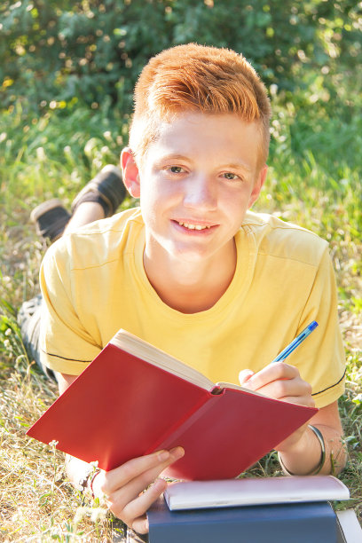 左撇子少年躺在草地上，写字、看书。图片下载