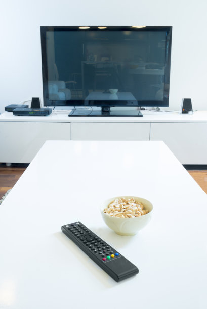 白色客厅里放着带遥控器和腰果的大屏幕电视图片下载