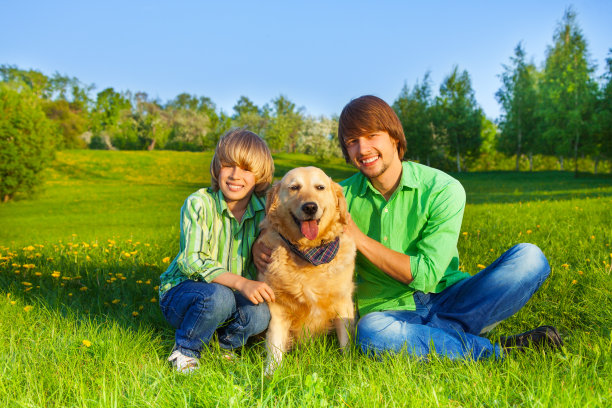 快乐的孩子，父亲和狗坐在公园的草地上图片下载