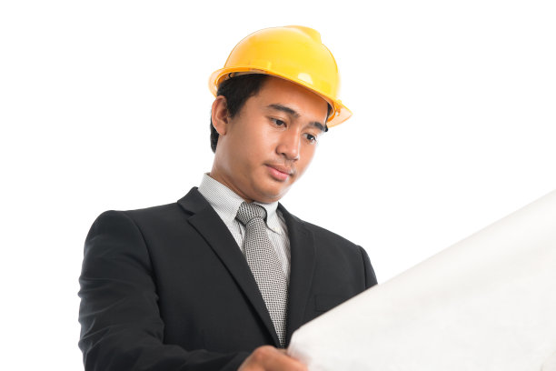 亚洲男性戴着黄色安全帽，看着蓝色印刷纸。图片下载