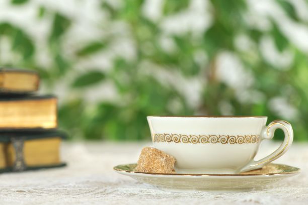 白色的茶杯，金色的装饰在复古的桌布上，以绿色的树叶和书籍为背景图片下载