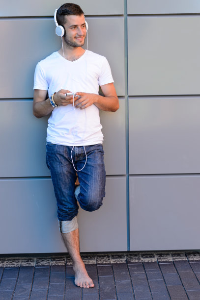 面带微笑的男生戴着耳机靠在墙上图片下载