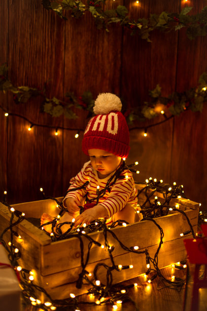 可爱的孩子坐在盒子里，包裹在圣诞彩灯里素材图片