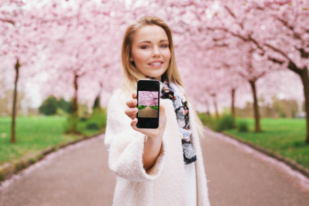 年轻女子在她的手机上展示春天公园的照片图片下载
