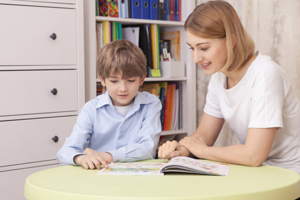 可爱的白人男孩坐在书桌前读课本。图片下载