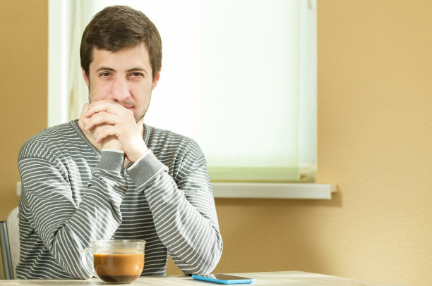 一个人坐在桌子旁。旁边放着电话和咖啡。图片下载