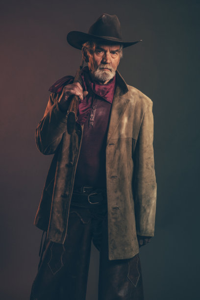 留着灰胡子，戴着棕色帽子，手持步枪的高级牛仔。图片下载