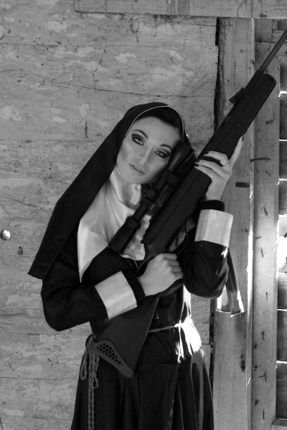 漂亮认真愤怒的尼姑拿着步枪，拿着枪。一个拿着枪的女孩的照片。危险的修女拿着枪。图片下载