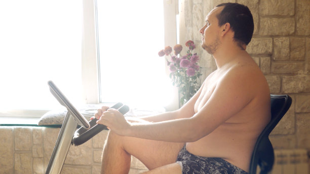 超重男子在自行车模拟器上锻炼，赤裸上身图片下载