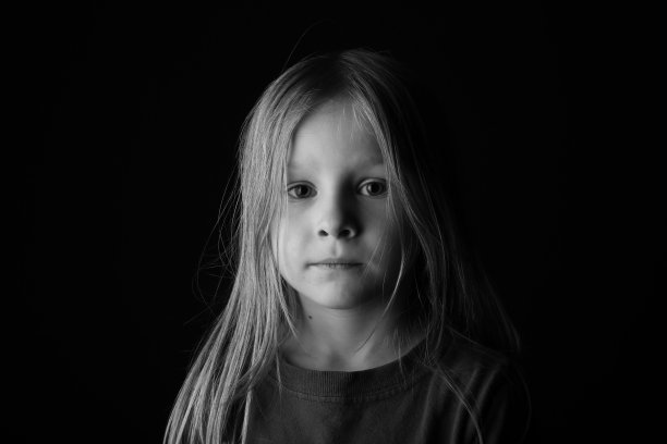 一个7岁的男孩长头发看起来严肃的黑色背景。图片下载