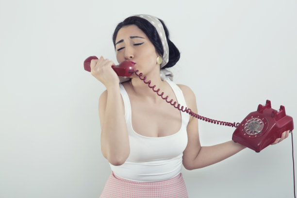 半身肖像的周到时尚的年轻女子在复古的服装与复古的电话工作室背景图片下载