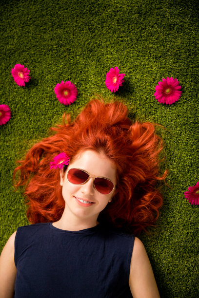 红发女孩戴着太阳镜躺在花园里的草地上图片下载