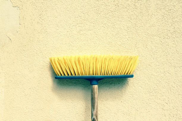 黄色推扫帚在质朴的淡黄色墙上图片下载