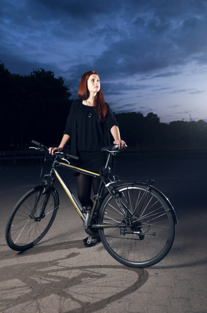 年轻女子晚上站在她的自行车旁图片下载
