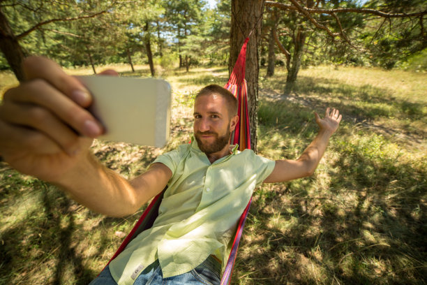 夏天，一名男子在吊床上放松，用手机自拍图片下载