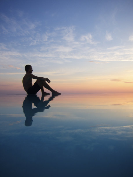 夕阳下无限水池中倒影的人的剪影图片下载