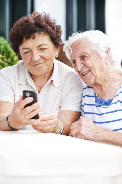 两个微笑的老年妇女使用手机图片下载