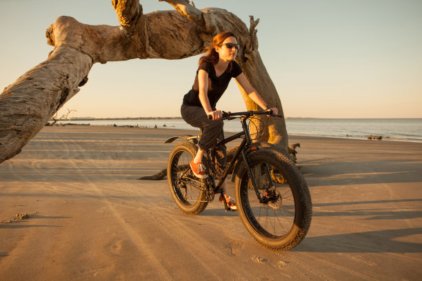 日出时，一个女人在海滩上骑山地车图片下载