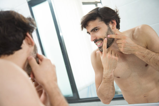 镜子里的年轻人在挤青春痘。图片下载