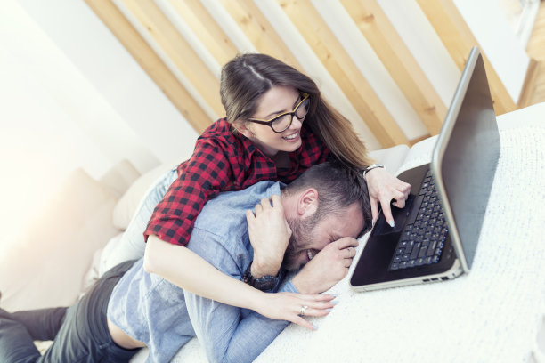 微笑的夫妇在家里为笔记本电脑争吵图片下载