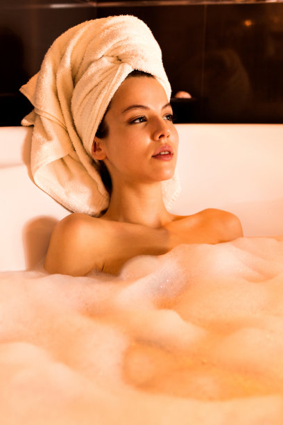沉思的女人在泡泡浴中放松，看着别处。图片下载