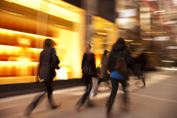 黄昏时，模糊的购物者经过灯火通明的商店橱窗图片下载