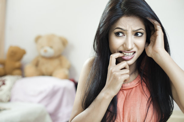 可爱的亚洲年轻女子咬她的指甲和看别处。图片下载