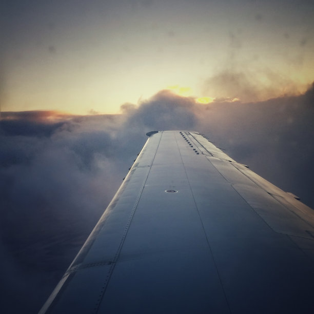 日出时，飞机机翼从浮云中升起图片下载