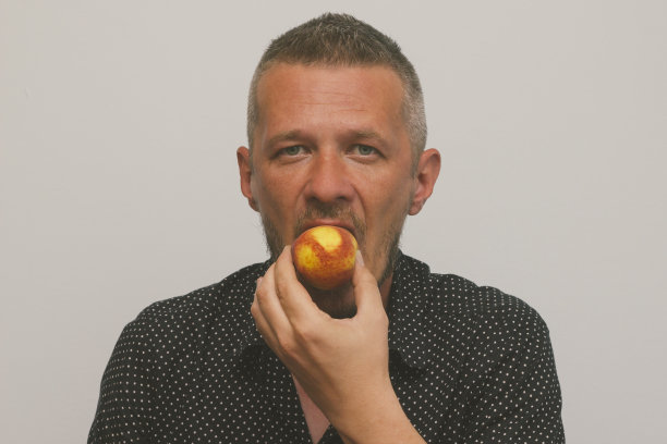 一个人正在吃红色、多汁、新鲜的桃子。近距离图片下载