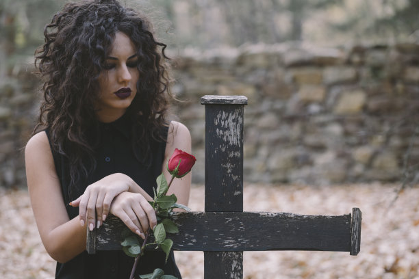 黑发女孩拿着红玫瑰，旁边是墓地的十字架图片下载