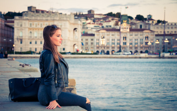 一个女人坐在里雅斯特的码头上，看日落图片下载