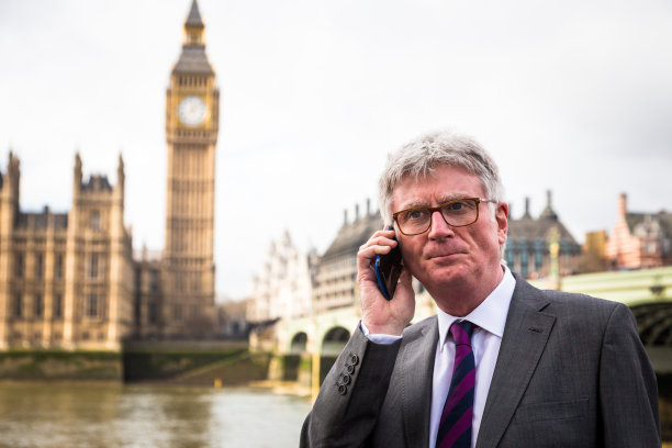 英国伦敦，戴着眼镜，穿着西装，在威斯敏斯特桥上打电话的年长商人图片下载