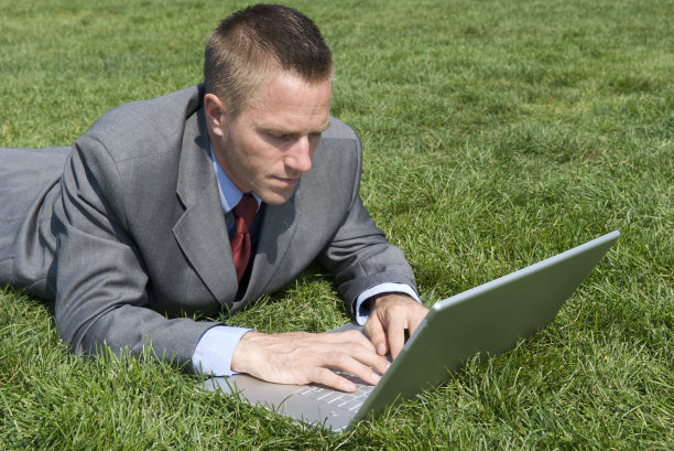 商人躺在草地上，拿着笔记本电脑图片下载