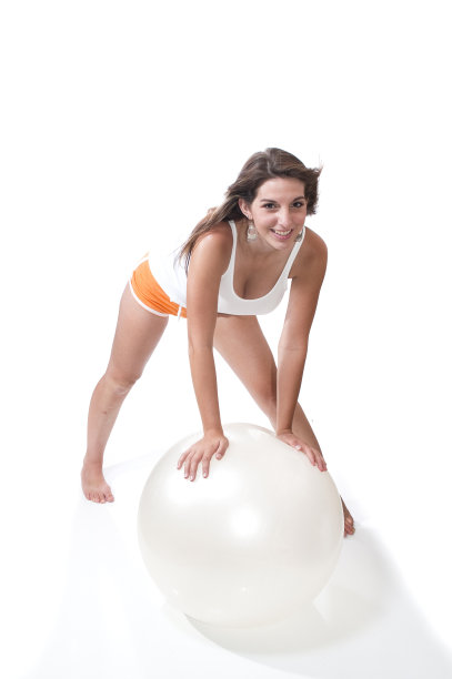 漂亮年轻的成年女人在白色的健身球上玩。图片下载