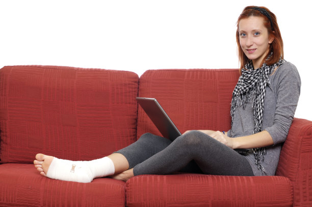 女孩在沙发上用PC和脚踝绷带图片下载