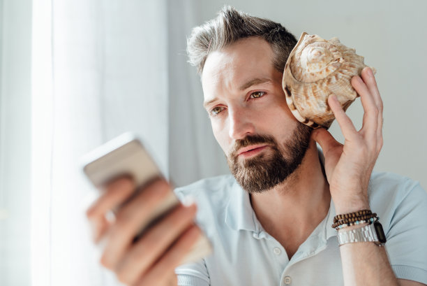 漂亮的男人拿着智能手机，在耳朵边听着炮弹图片下载