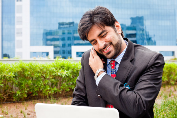 年轻的亚洲印度商人使用笔记本电脑和打电话图片下载