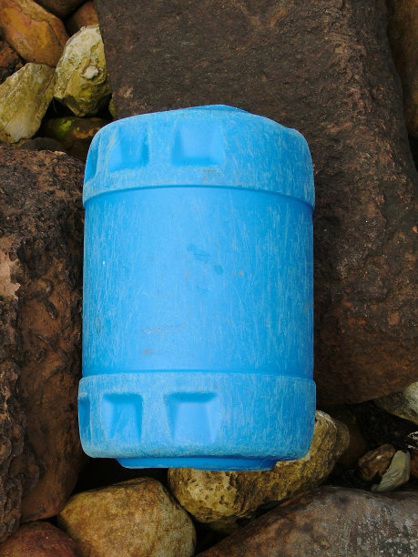 丢弃的蓝色塑料桶上的岩石。图片下载