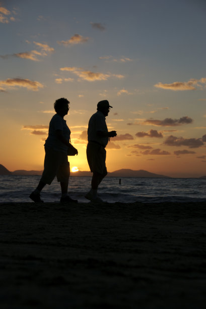 老年夫妇的剪影走过金色的热带日落海滩图片下载