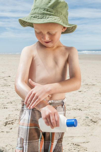 小男孩在海滩上涂防晒霜。图片下载